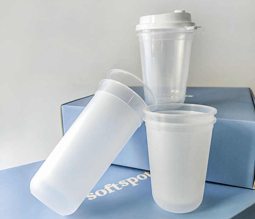 Three transparent plastic cups of different sizes and shapes, one with a white plastic lid, placed on a blue box